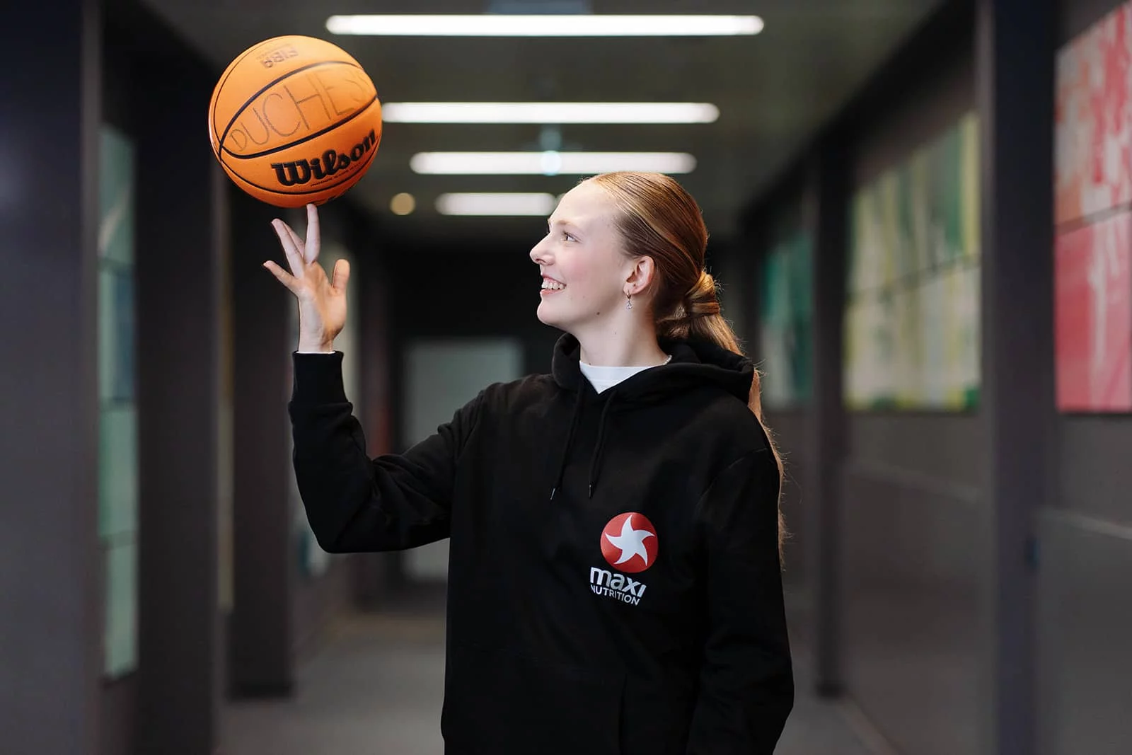 Mentorin feuert lächelnd ein junges Basketballtalent beim Dribbling in einer Sporthalle an